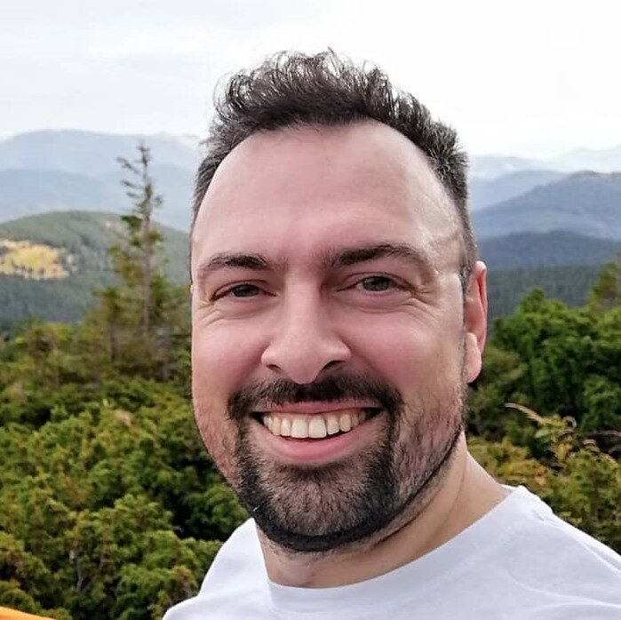 Mykola Vorobiov, smiling, photographed outdoors against forested mountains.